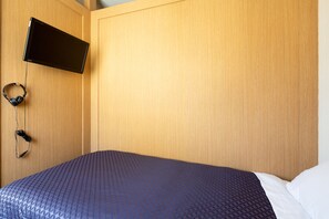Quarto de hotel com uma cama, televisão fixada na parede e auscultadores pendurados na parede.