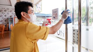 A person cleaning a glass door with a spray bottle and cloth. - Blitz Hotel Batam Centre (Batam)