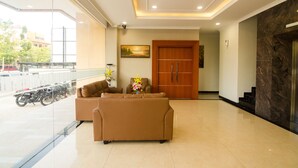 A hotel lobby with a sofa, a wooden door, and a view of parked motorcycles outside. - Blitz Hotel Batam Centre (Batam)