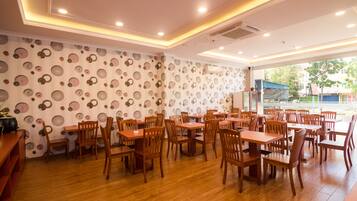 A restaurant with wooden tables and chairs, patterned wallpaper, and a view of the outside.