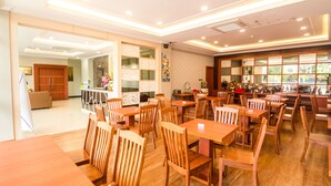 A restaurant with wooden tables and chairs, a kitchen area, and a view through the window. - Blitz Hotel Batam Centre (Batam)