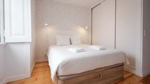 A bedroom with a bed, bedside lamps, a wooden floor, and a wardrobe.