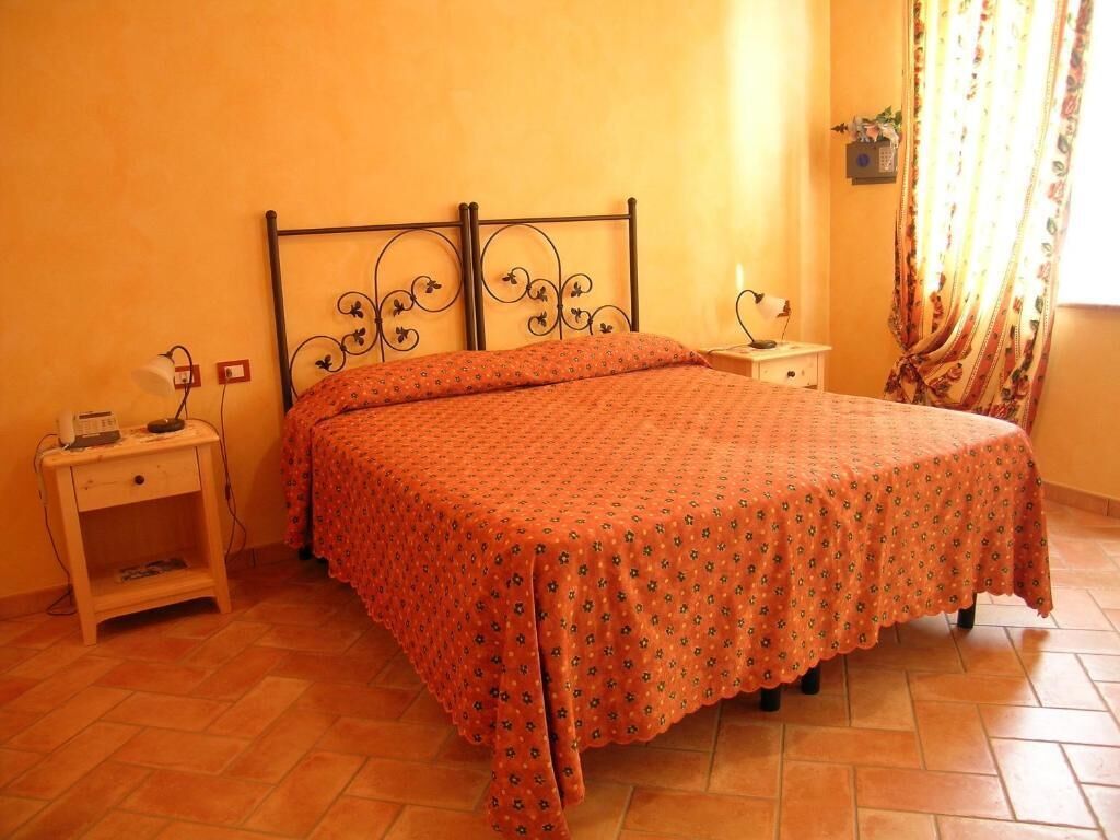 Un dormitorio con cama, mesitas de noche, una lámpara y un ventanal con cortinas.