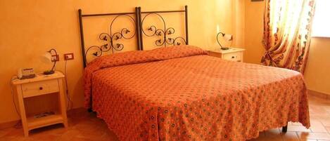 Un dormitorio con cama, mesitas de noche, una lámpara y un ventanal con cortinas.