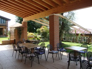 An outdoor patio area with a wooden pergola, brick pillars, and a variety of seating arrangements including tables and chairs. - Agriturismo Le Tese (Lazise)