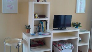 A living room with a TV, books, and a small plant on a white shelf.