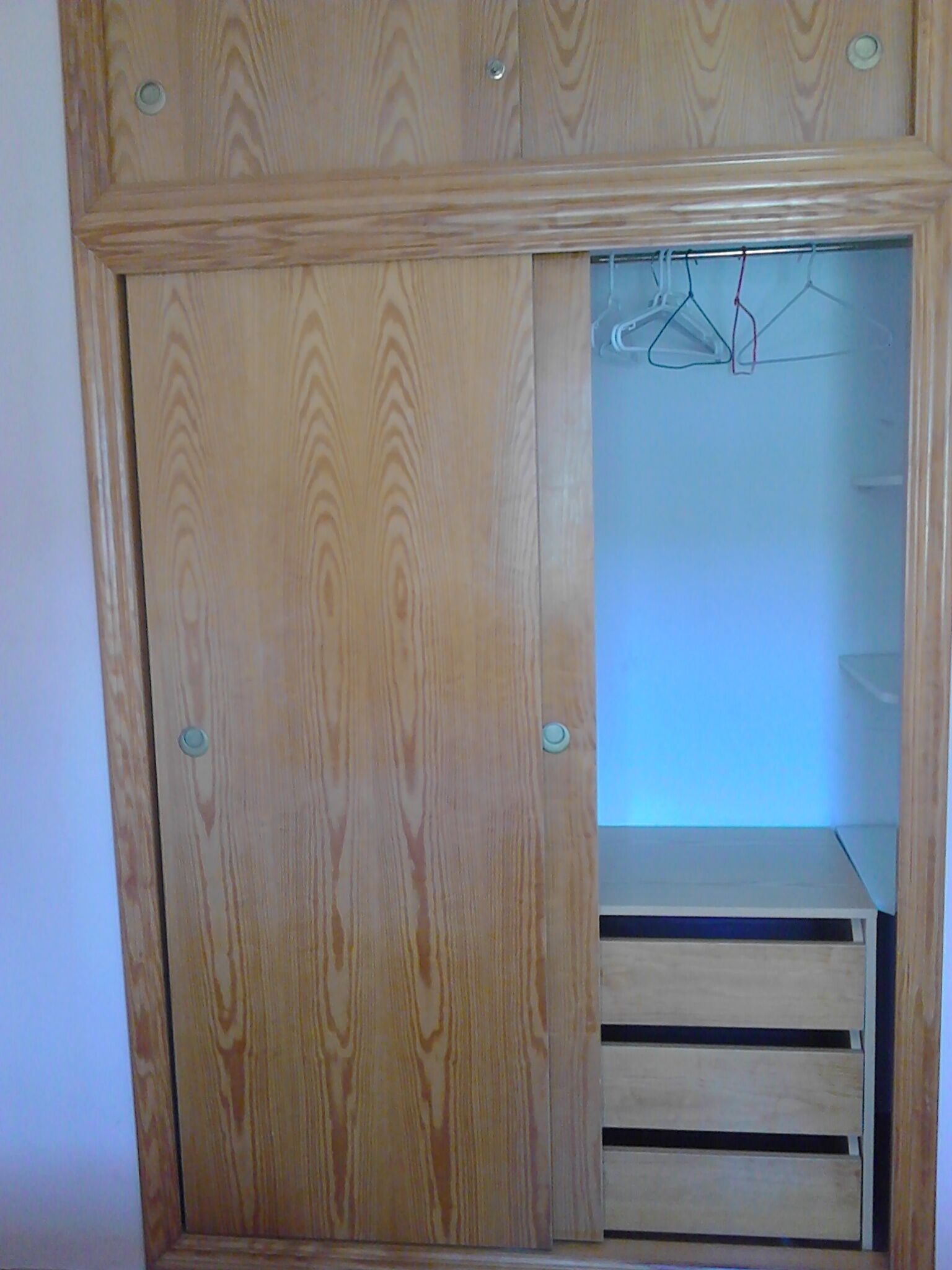 Un armario de madera con puerta espejada y una repisa pequeña.