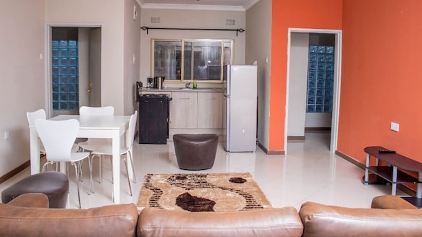 A modern living room with a dining area, kitchen, and orange accent wall. - Rose Villa Lodge (Kitwe)