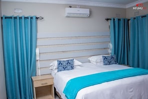 A bedroom with a bed, curtains, a nightstand, and an air conditioning unit.
