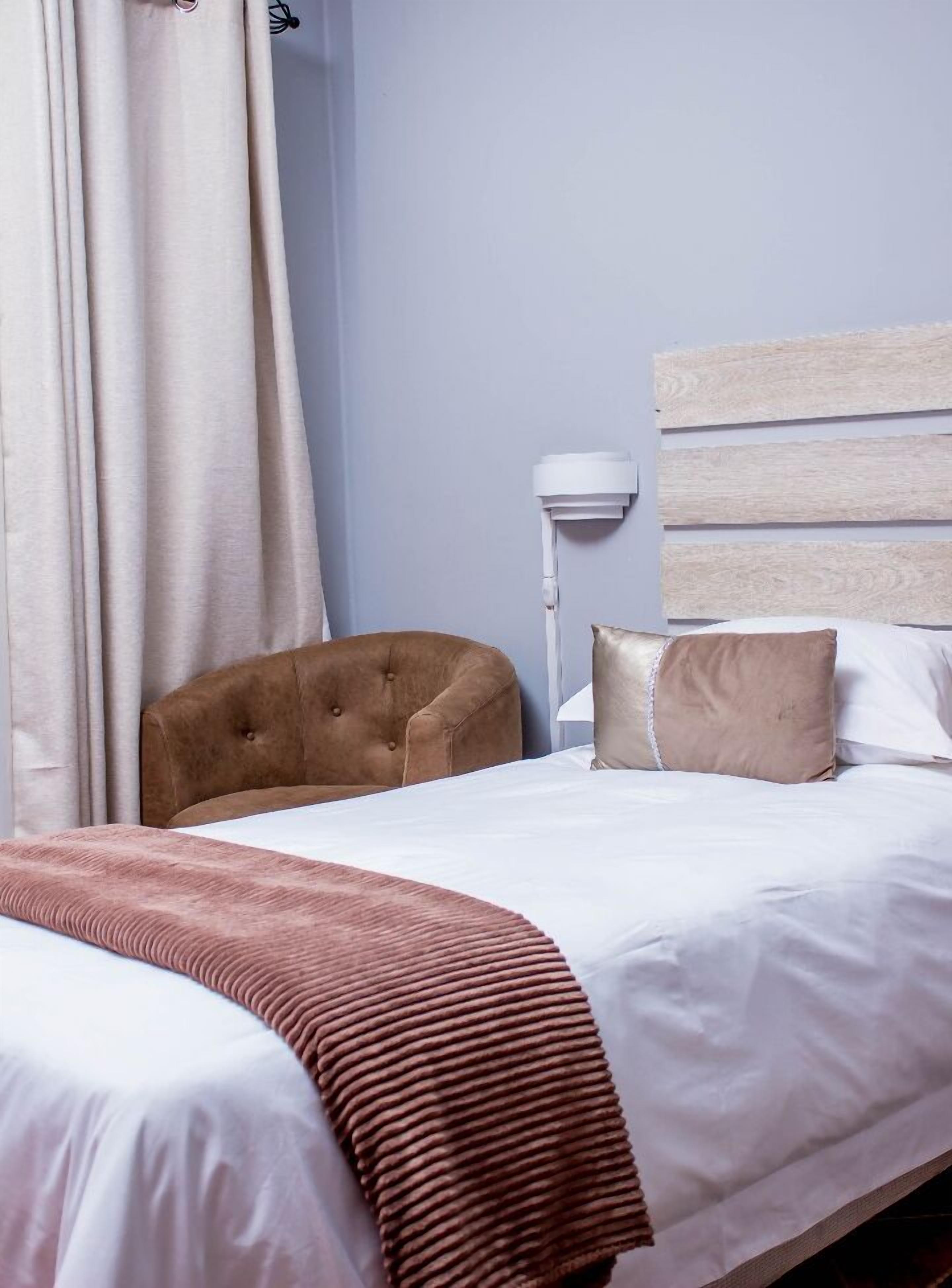 A hotel room with a bed, a headboard, a bedside lamp, a chair, and a window with curtains.