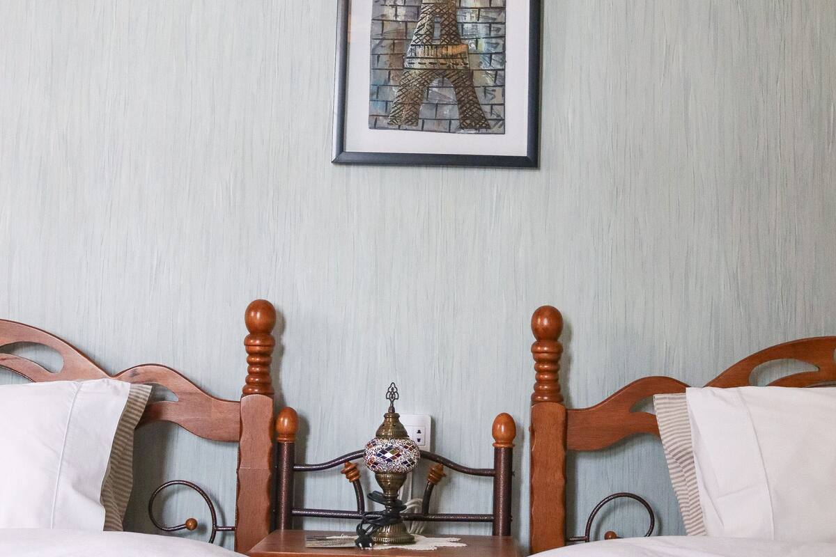 A hotel room with two wooden beds, a nightstand with a lamp, and a framed picture of the Eiffel Tower on the wall.