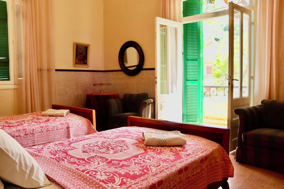 A hotel room with two beds, a round mirror, a small table, and a view of the outside.