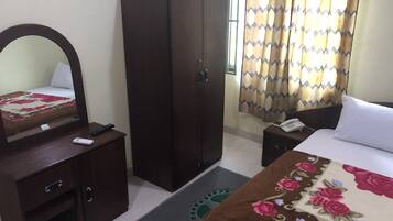 A hotel room with a bed, a wardrobe, a bedside table with a phone, a mirror, and a desk with a remote control.