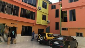 A multi-story building with a yellow and orange facade, large windows, and parked cars. - Ricardo's property (Accra)