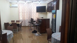 A dining area with a table and chairs, a refrigerator, a television, and a ceiling fan. - Ricardo's property (Accra)