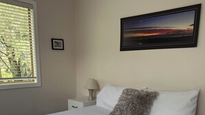 Una cama bien hecha con un edredón verde, un cuadro en la pared y una ventana con persianas.