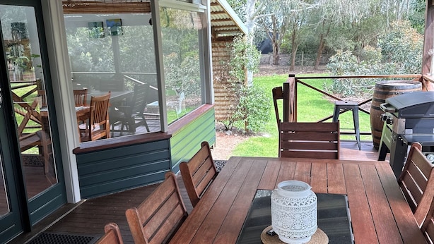 Un patio exterior con mesa y sillas de madera, y un farol decorativo.