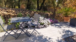 An outdoor seating area with a table and chairs, surrounded by a stone wall and various plants. - Homerez - House in Mornas (Mornas)