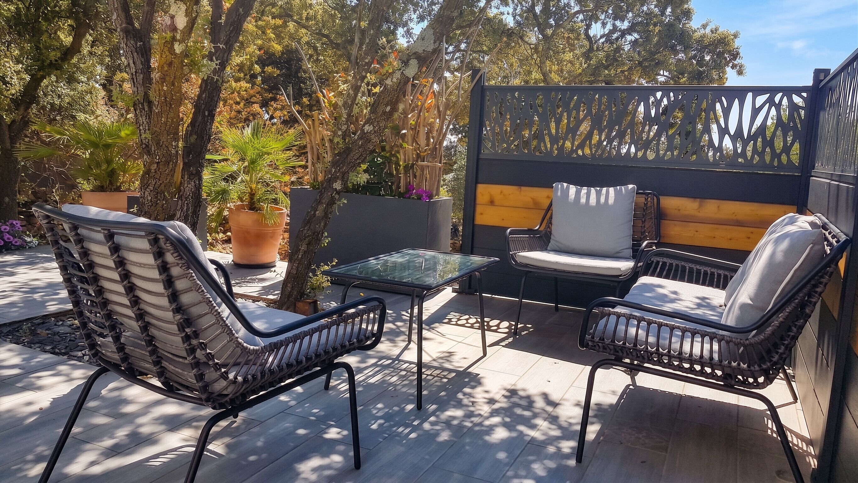 An outdoor patio with wicker chairs, a glass table, and a wooden fence.