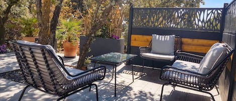 An outdoor patio with wicker chairs, a glass table, and a wooden fence.