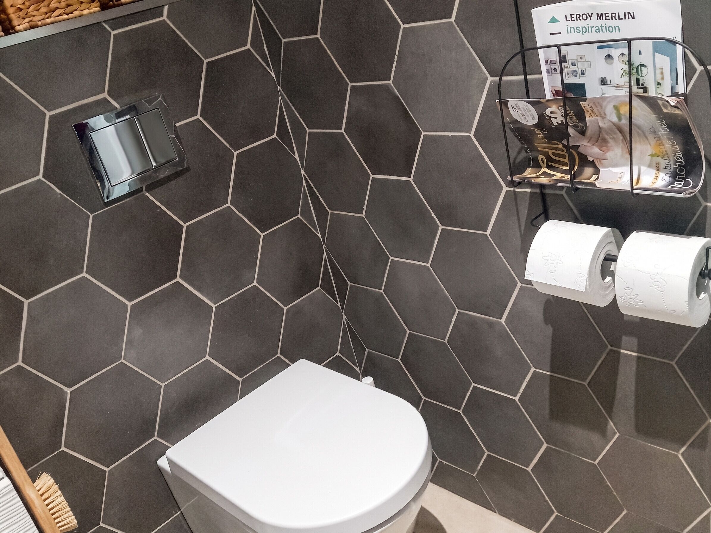 A bathroom with a hexagonal tile pattern, a toilet, a hand dryer, and a toilet paper holder.