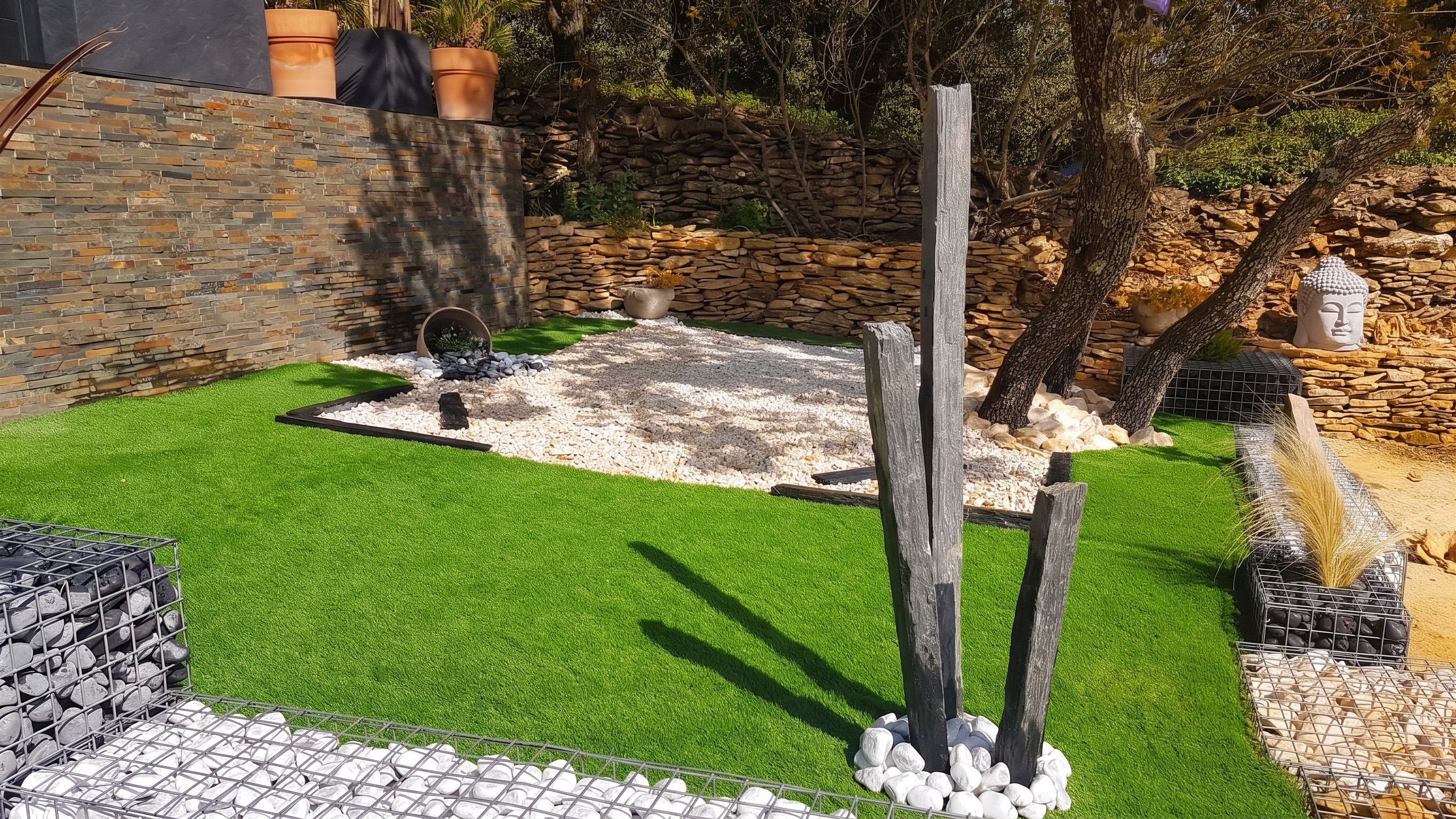 Un jardin aménagé avec du gazon synthétique, des murs en pierre et une variété de plantes.