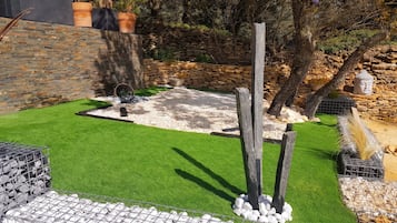 Un jardin aménagé avec du gazon synthétique, des murs en pierre et une variété de plantes.