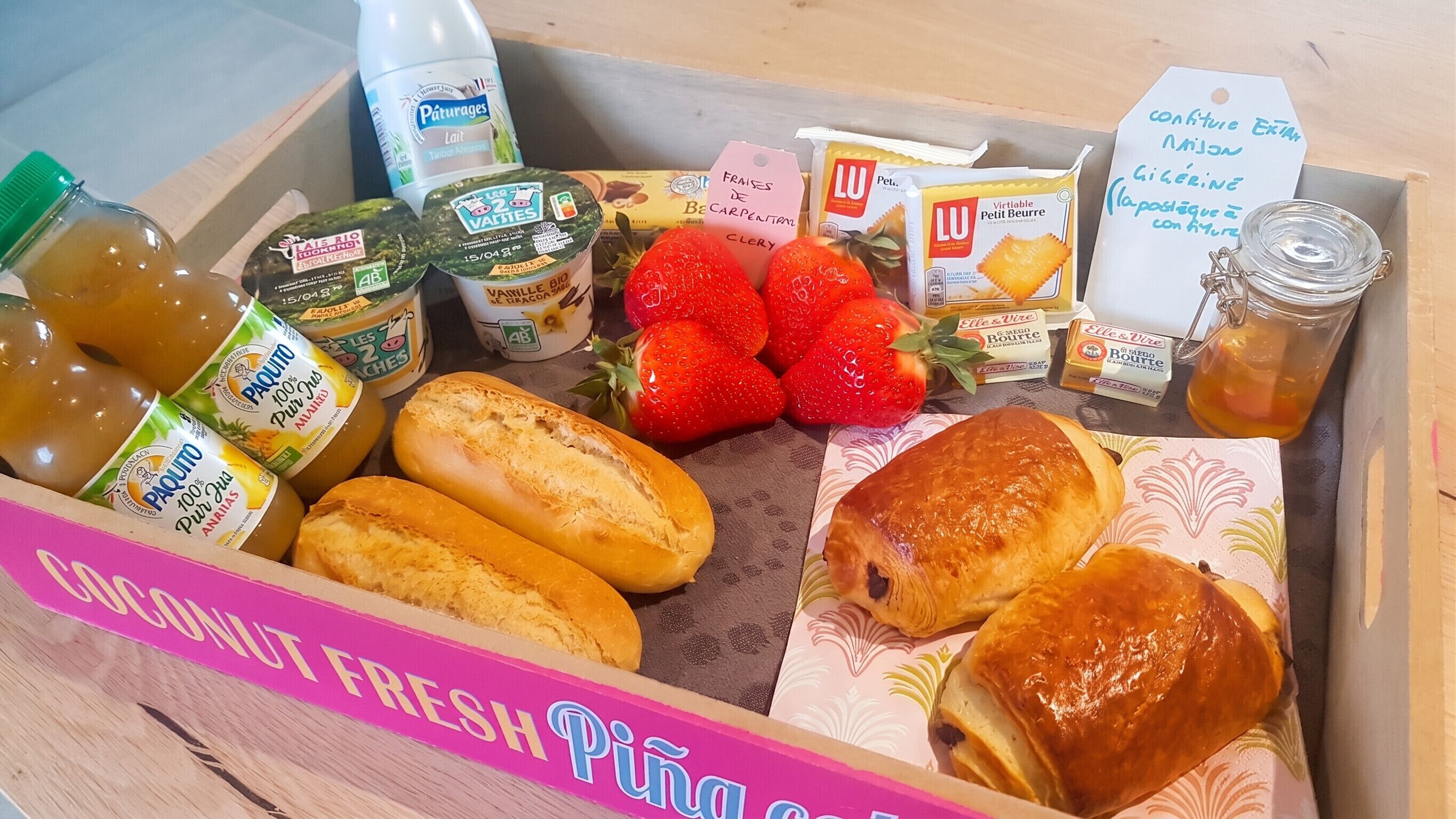 Diverse etenswaren, zoals brood, aardbeien en drankjes, in een doos met de tekst 'Loconut Fresh Pinga'.