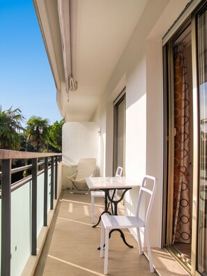 A balcony with a table and chairs, a sliding glass door, and a view of palm trees. - Homerez - Apartment in Antibes (Antibes)