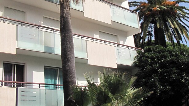 A multi-story building with balconies, palm trees, and a hedge in front. - Homerez - Apartment in Antibes (Antibes)