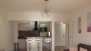 A modern kitchen with three bar stools, a dining table, and a chandelier. - Homerez - Apartment in Antibes (Antibes)