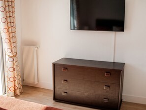 A room with a dark wooden dresser, a flat-screen TV mounted on the wall, and a radiator. - Homerez - Apartment in Antibes (Antibes)