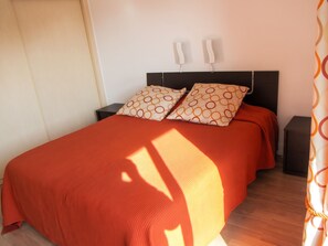 A bed with a red blanket and two patterned pillows, a bedside table, and a wall-mounted light fixture. - Homerez - Apartment in Antibes (Antibes)