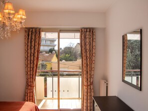 A bedroom with a balcony, a chandelier, and a view of buildings and trees. - Homerez - Apartment in Antibes (Antibes)