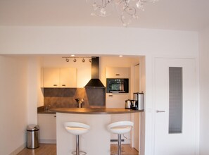 A modern kitchen with a central island, bar stools, a coffee machine, and a microwave. - Homerez - Apartment in Antibes (Antibes)