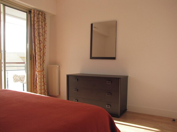A bedroom with a bed, a dresser, a radiator, and a window with curtains. - Homerez - Apartment in Antibes (Antibes)