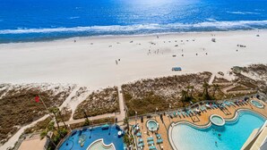 Vista aérea de un complejo turístico en la playa con piscina y gente disfrutando de la playa.