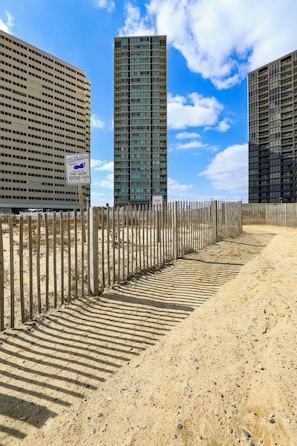 Un sentier sablonneux mène à une zone délimitée par une barrière, où un panneau indique l’emplacement d’une plage.