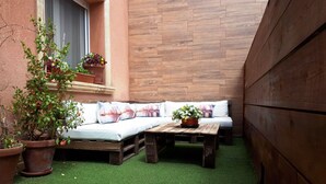 A cozy patio with a wooden bench, a cushioned seating area, and potted plants.