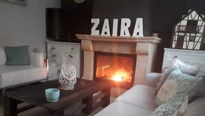 A cozy living room with a fireplace, a sofa, a coffee table, and a decorative sign that reads "ZAIRA".