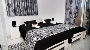 A bedroom with a bed, two pillows, a bedside table, a speaker, and curtains.