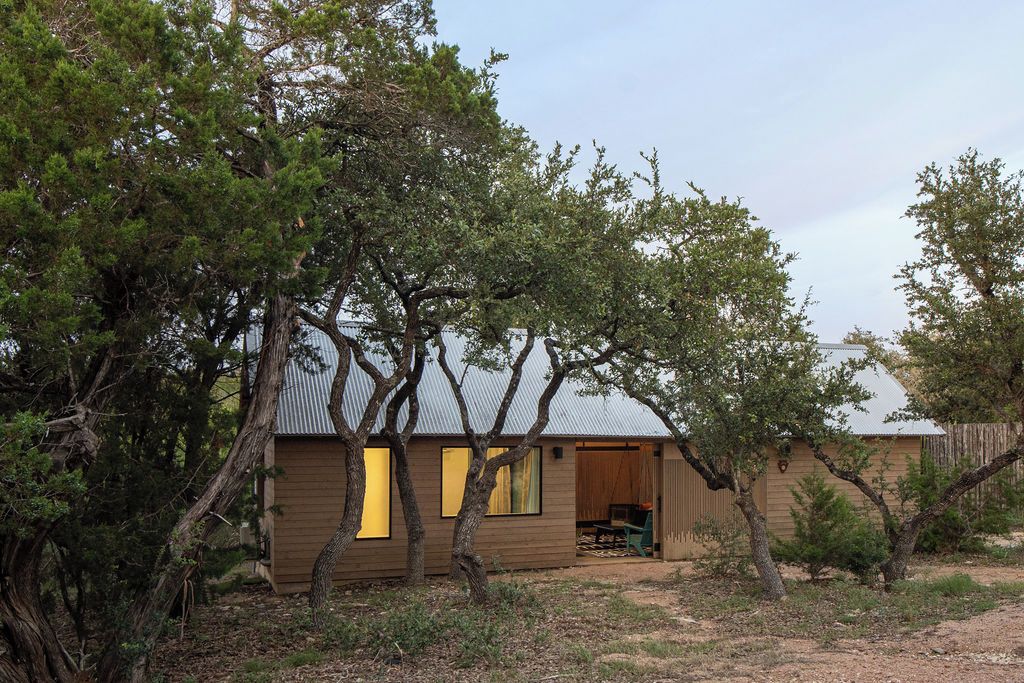 Un bâtiment d’un seul étage, doté d’un toit en pente, entouré d’arbres et d’arbustes.