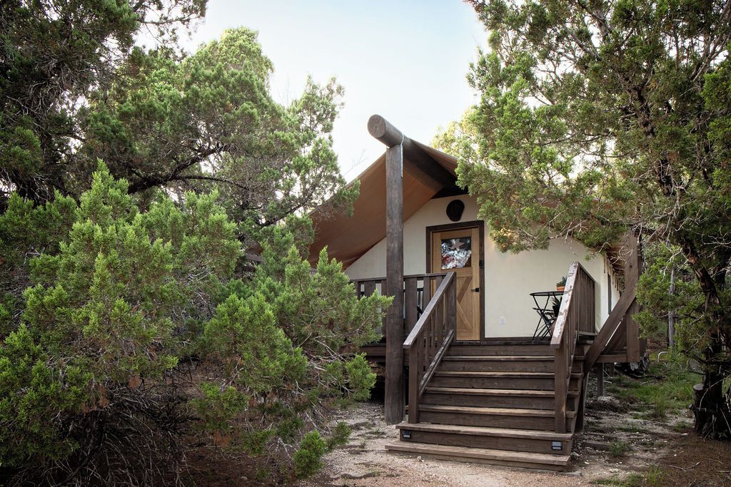 A rustic cabin with a wooden staircase leading to a door, surrounded by dense pine trees.