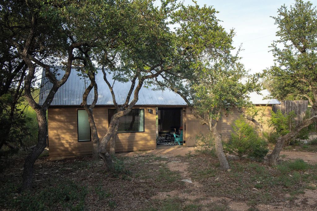Una casa de un piso con techo de lámina corrugada, rodeada de árboles y un sendero de tierra.
