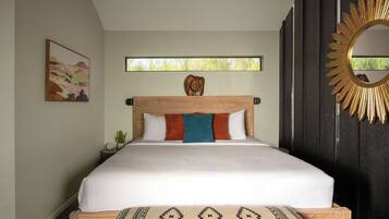 A bedroom with a large bed, a window, a wall-mounted mirror, and a painting.