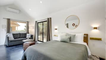 Een moderne slaapkamer met een groot bed, een bank en een eettafel. Er is een glazen schuifdeur die leidt naar een buitenruimte.