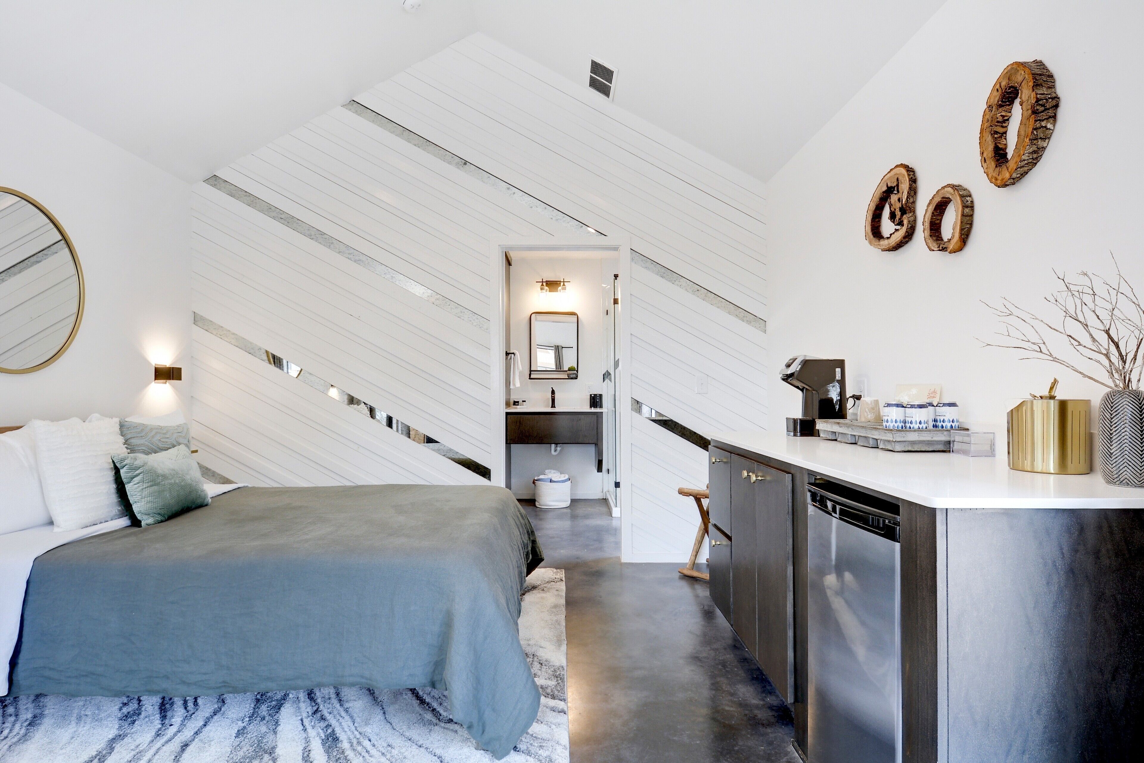A modern bedroom with a bed, bedside table, and a view into the kitchen area.
