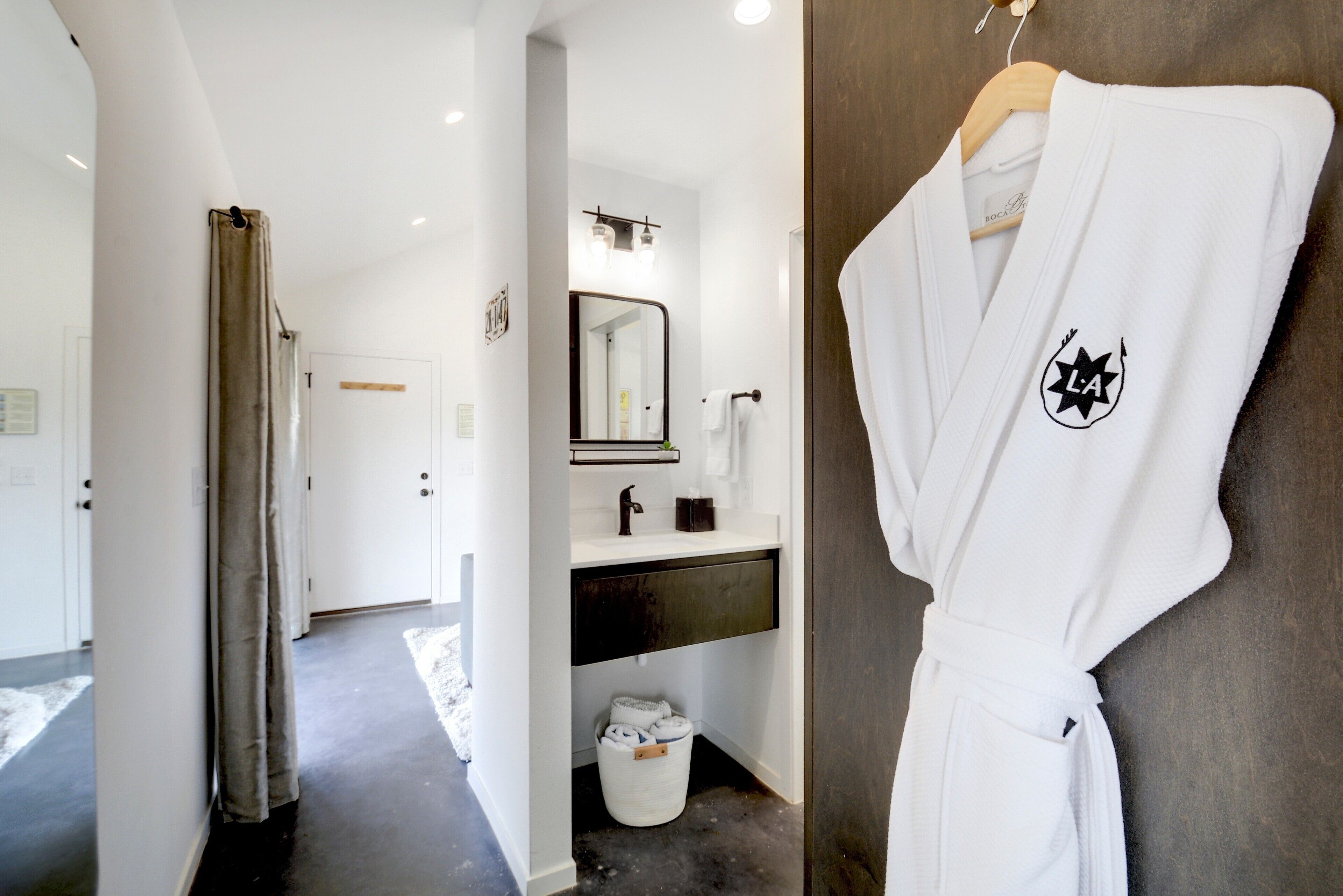Casa de banho de hotel com um roupão branco pendurado num suporte, uma pia com espelho e um porta-toalhas.