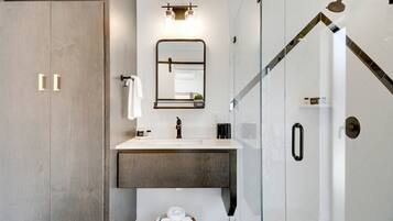 Une salle de bain moderne avec un grand miroir, un lavabo et un espace douche.