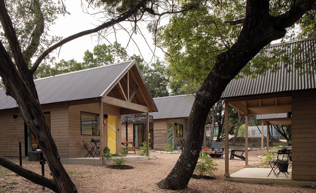 A wooden cabin with a covered patio area, surrounded by trees.
